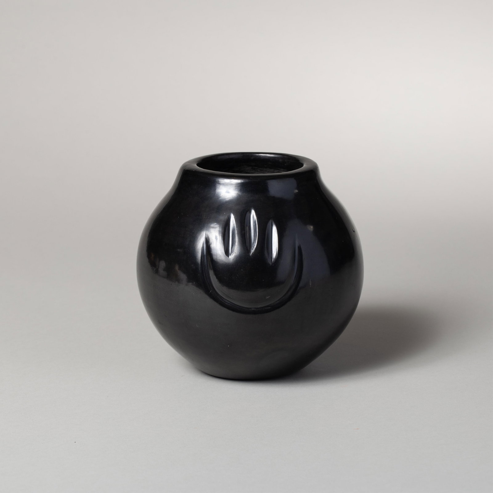 Angela Baca, Santa Clara Pueblo 1927-2014, Bear Paw Blackware Jar, Clay, 5 1/4 x 6 in. (13.3 x 15.2: Blackware jar of rounded form with broad shoulders and a slightly flared rim, the highly polished surface carved with a bear paw m otif encircling the body. Underneath the jar is signed "Angela Baca,