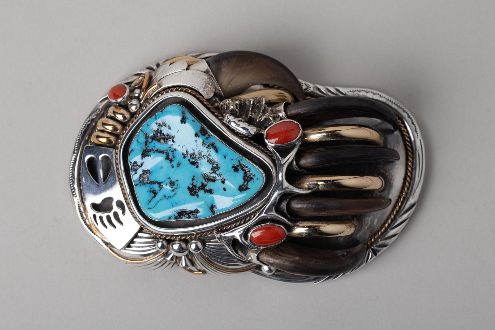 Joe Piaso Jr. Navajo Bear Claw, Turquoise, Coral, Sterling Silver & Gold Belt Buckle: Handcrafted Native American Sterling silver belt buckle marked by esteemed artist J Piaso Jr - a true statement piece of wearable art. The buckle features a dramatic central design of a bear paw, acce