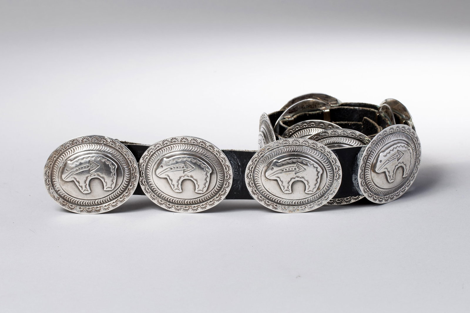 Navajo Sterling Silver Concho Belt with Bear Motif: Navajo sterling silver concho belt, composed of eleven oval conchos, each featuring a raised bear motif at center, surrounded by finely stamped borders with scalloped and linear elements. The conchos