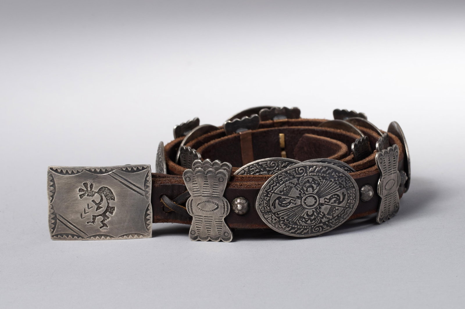 Kokopelli Buckle SS 9 Conchos 10 Butterflies Concho belt: Comprising nine oval conchos and ten butterfly spacers, each concho finely stamped with radiating and segmented motifs incorporating stylized Kokopelli figures. The terminals feature a rectangular buc
