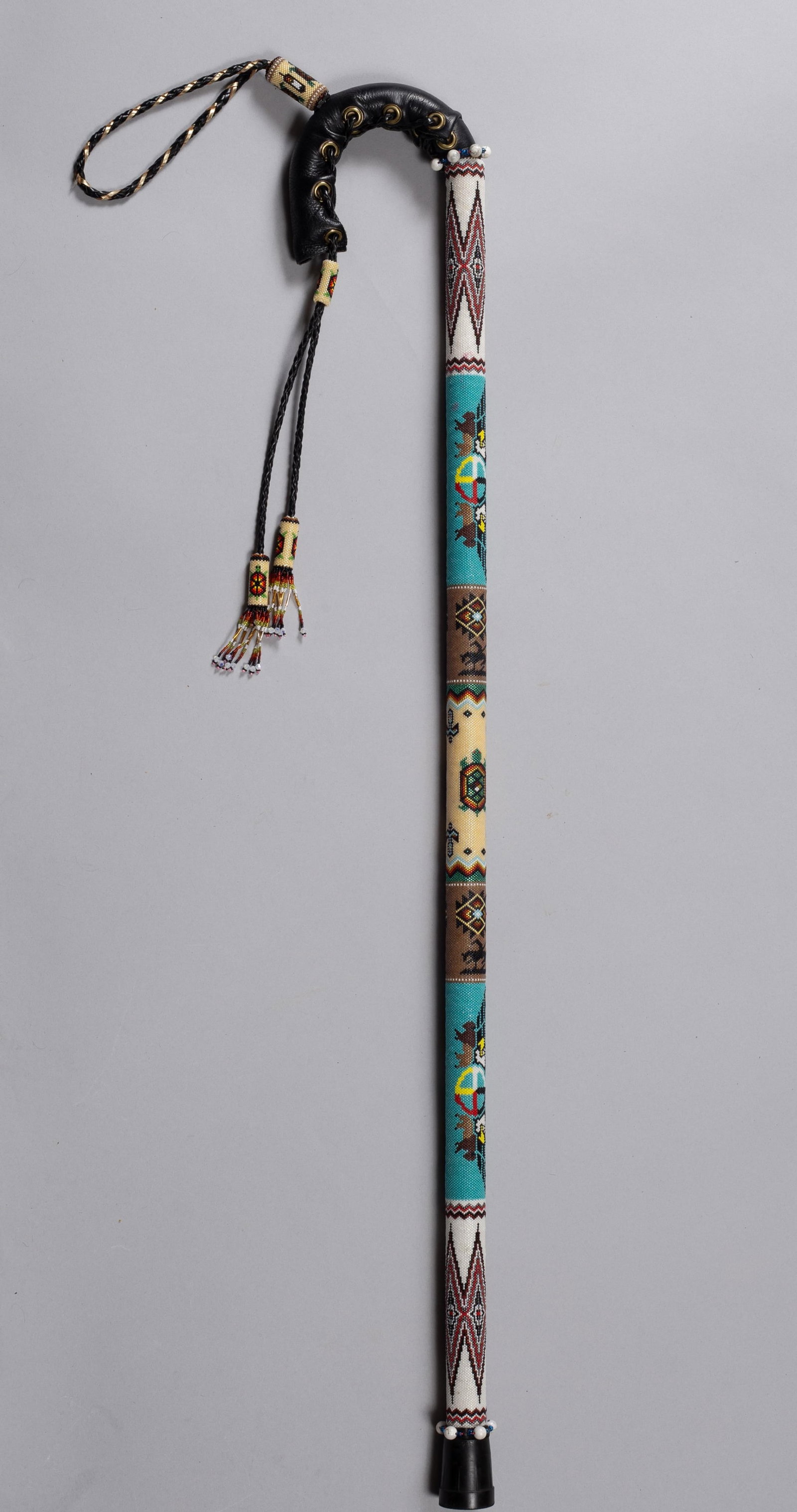 Plains Beaded Cane: Plains beaded cane, likely mid-late 20th century, the wood shaft fully wrapped in multicolored glass seed beadwork depicting geometric and pictorial motifs, including avian and symbolic elements, on b