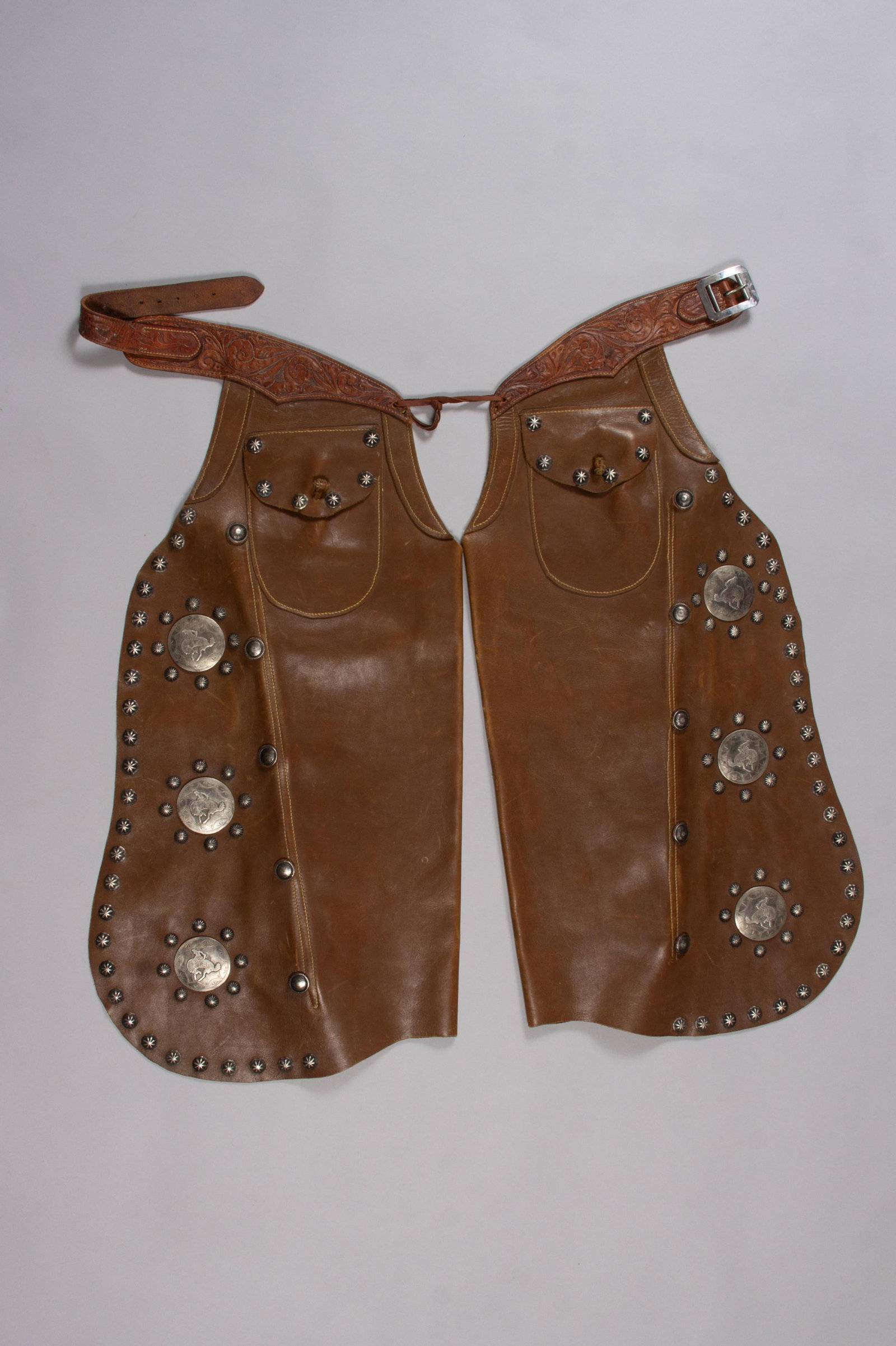 Edward H. Bohlin Brown Batwing Chaps with Sterling Silver Conchos: Marked "Edward H. Bohlin, Hollywood CA" three times (Belt and Buckle). These parade chaps are crafted from rich brown leather and adorn with domed sterling silver conchos down each leg and on the carv