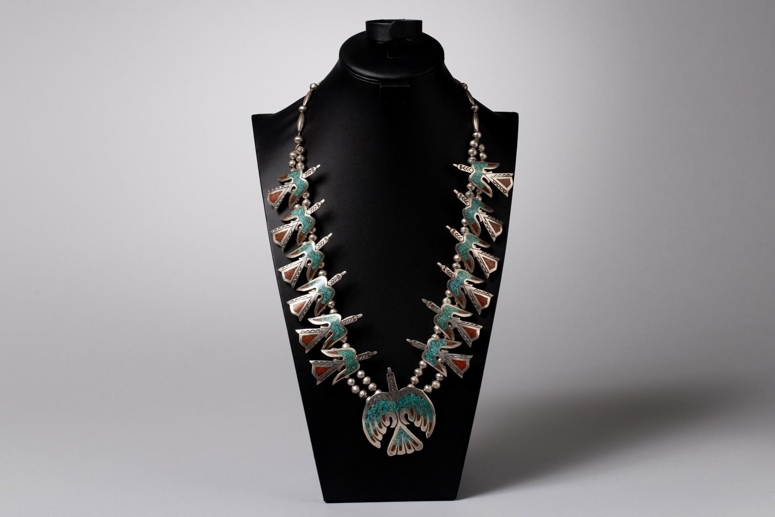 William Singer Navajo Peyote Bird (or Water Bird) Squash Blossom Necklace: A Southwestern squash blossom layout, substituting traditional blossoms with multi-link figural birds. The birds feature turquoise and coral chip inlay techniques. This distinctive method—pioneered 
