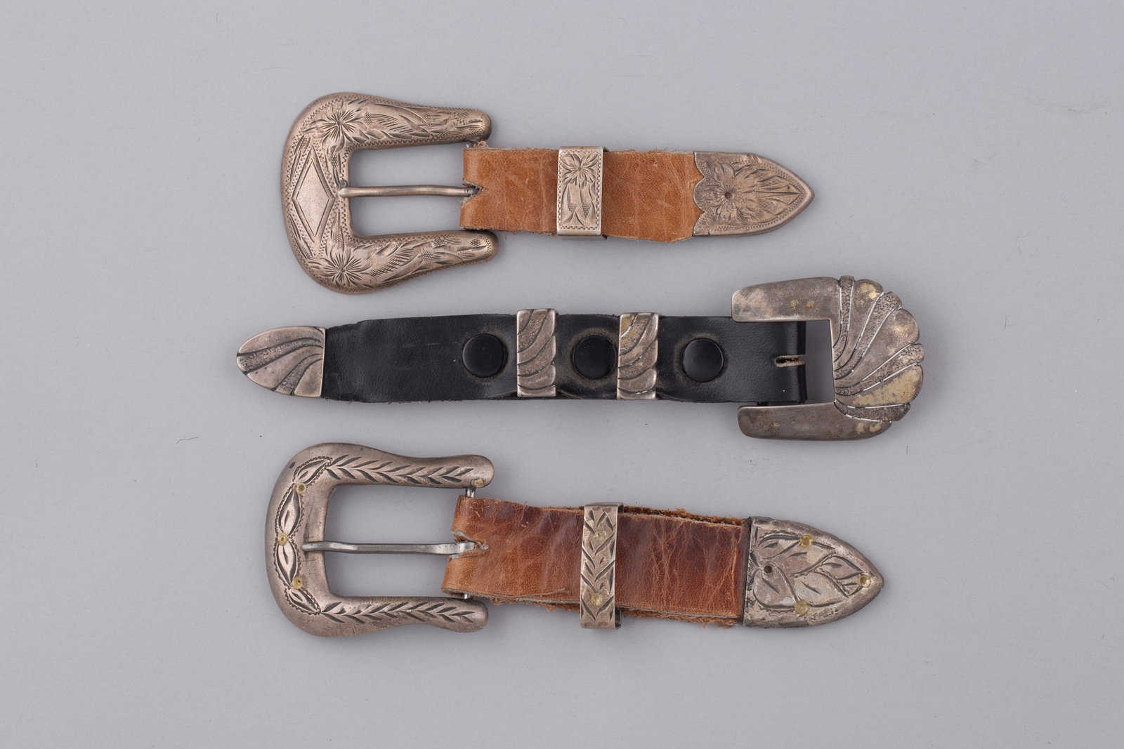 Three Silver Western Buckles, Keepers & Tips (Ranger sets): Three sterling silver Western style buckles, keepers, and tips (Ranger sets), including two engraved sterling buckle and tip sets with matching keepers mounted on brown leather tabs, and one sterling 