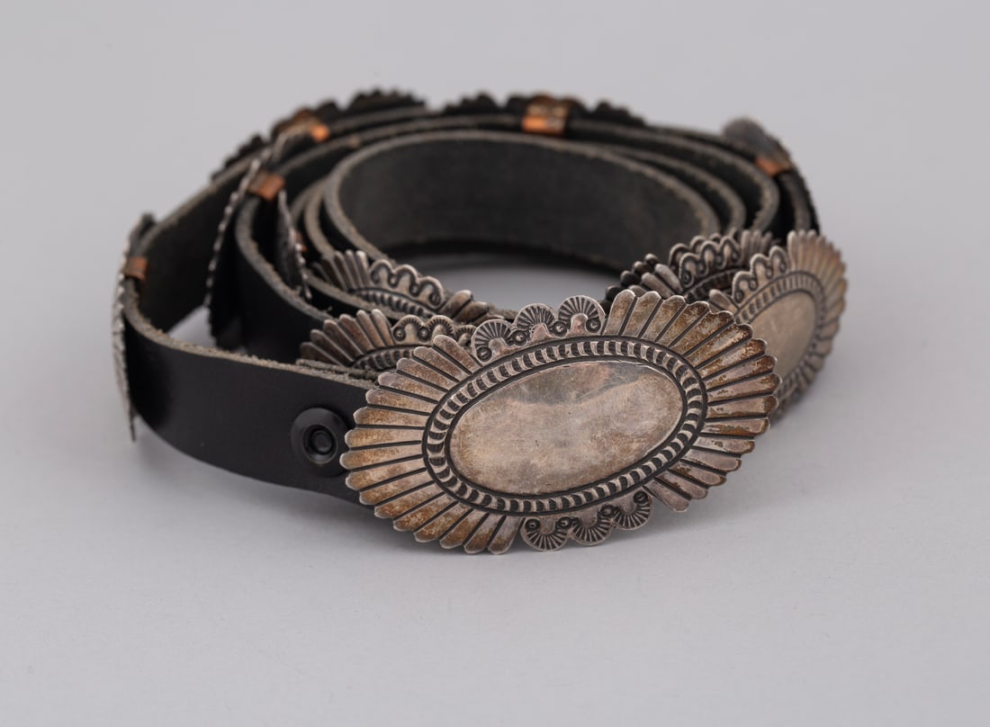 Vintage Petite Sterling Silver Concha Belt: The belt features a series of intricately detailed, petite oval conchas mounted seamlessly along a classic dark leather strap. Each concha showcases expert craftsmanship, complete with hand-stamped ge