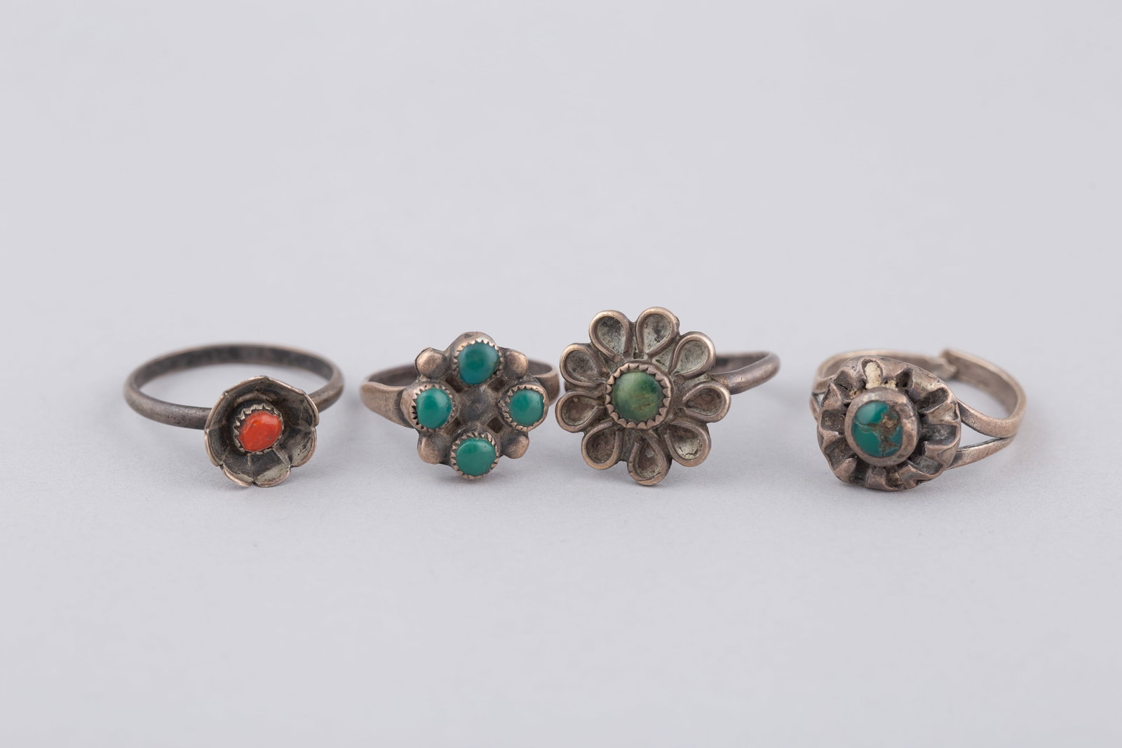 Four Petite Floral Design Native American Turquoise and Coral Rings: A charming collection of four petite Southwestern rings showcasing traditional Native American floral craftsmanship. Fabricated in sterling silver, the group features classic cluster-work and stylized