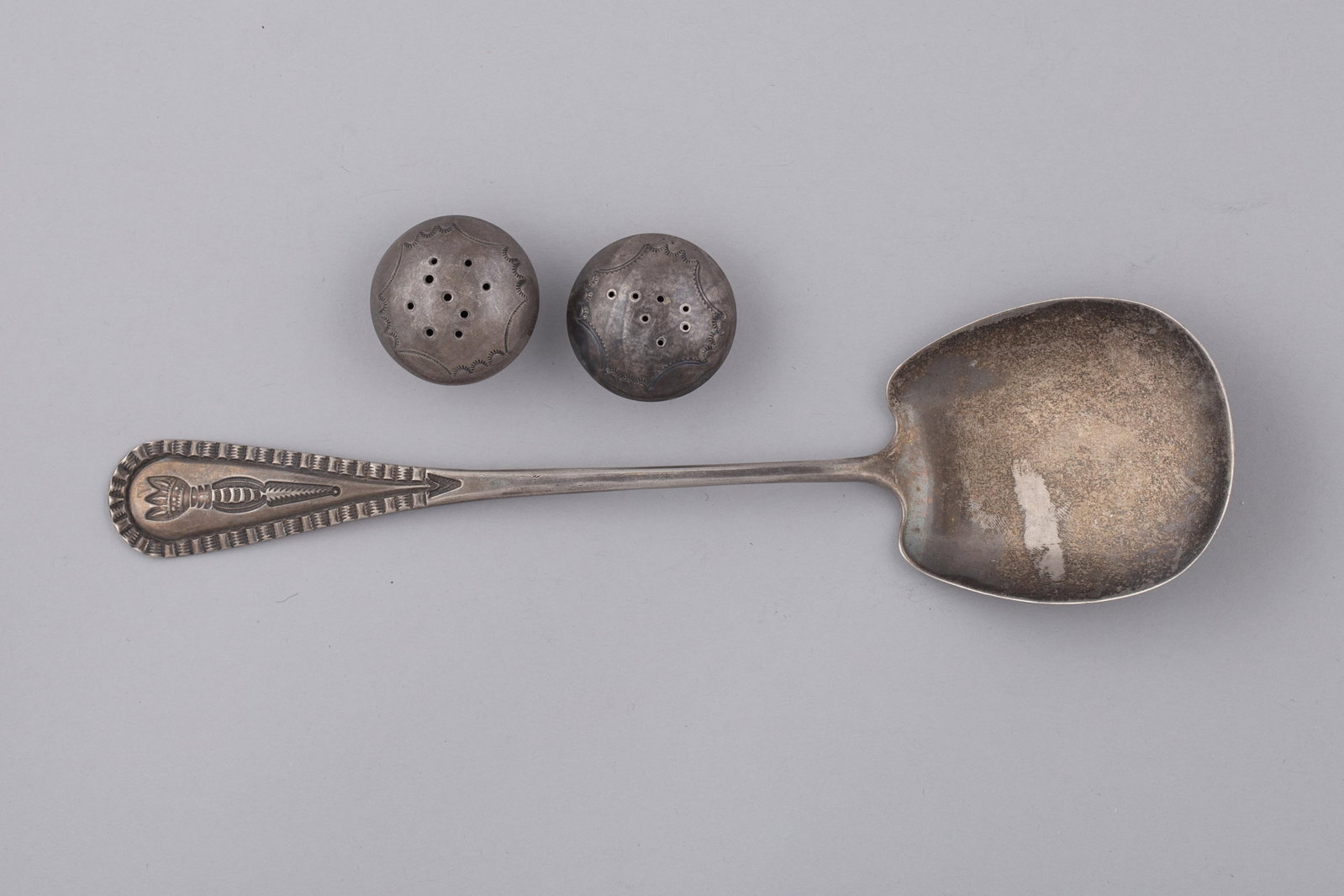 Vintage Navajo Silver Serving Spoon and Salt and Pepper Shaker: Navajo silver serving spoon with a hand-stamped handle featuring a central arrow motif bordered by geometric decoration and scalloped edging. The spoon has a broad, rounded bowl and a tapered handle