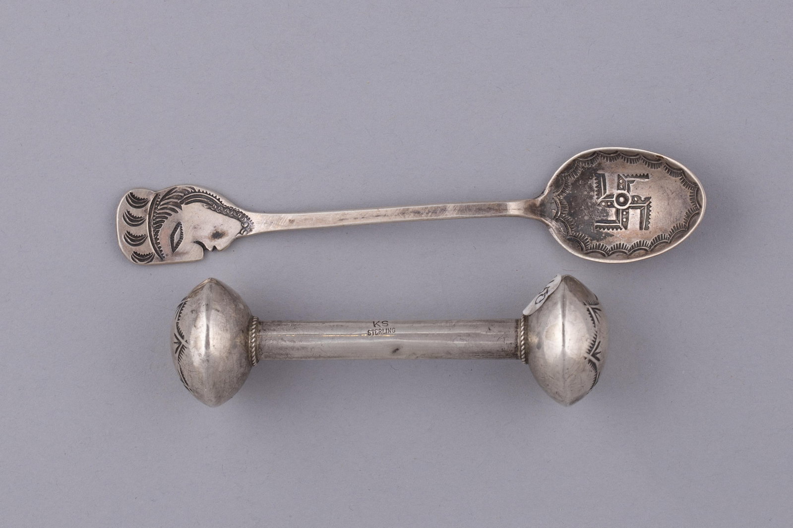 Two Navajo Silver Objects: Navajo Profile Demitasse Spoon and Navajo Sterling Silver Baby Rattle: A charming and highly collectible two-piece set of historic Southwestern silver, featuring an antique Navajo sterling silver baby rattle and a Profile spoon. Crafted with traditional techniques, these