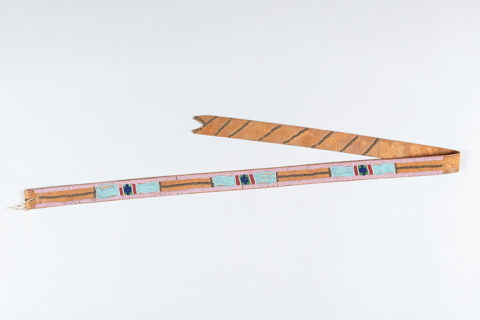 Crow Leather Belt with Drop, c. 1870-1880: A fine and rare 19th-century harness leather belt featuring a distinctive "split belt drop". This piece is representative of the sophisticated Crow geometric style, characterized by its balanced use