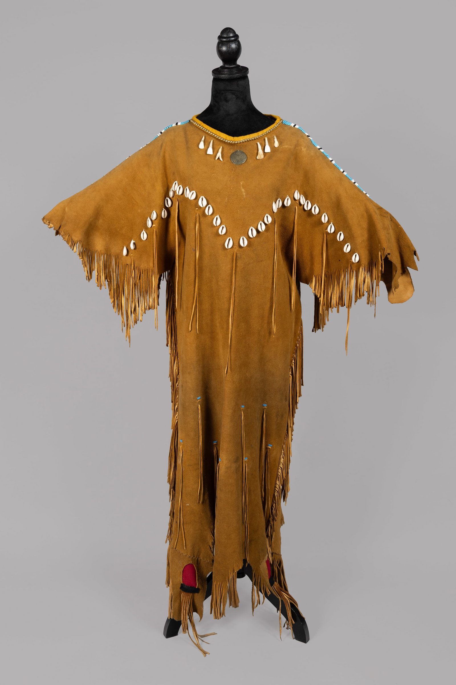 Vintage Plains-Style Buckskin Ceremonial Dress and Catalogued and Photographed Collection of works: This finely crafted buckskin ceremonial dress features long, hand-cut fringe and is adorned with rows of cowrie chells arranged in a traditional V-shaped "yoke" pattern on the bodice. The sleeves and