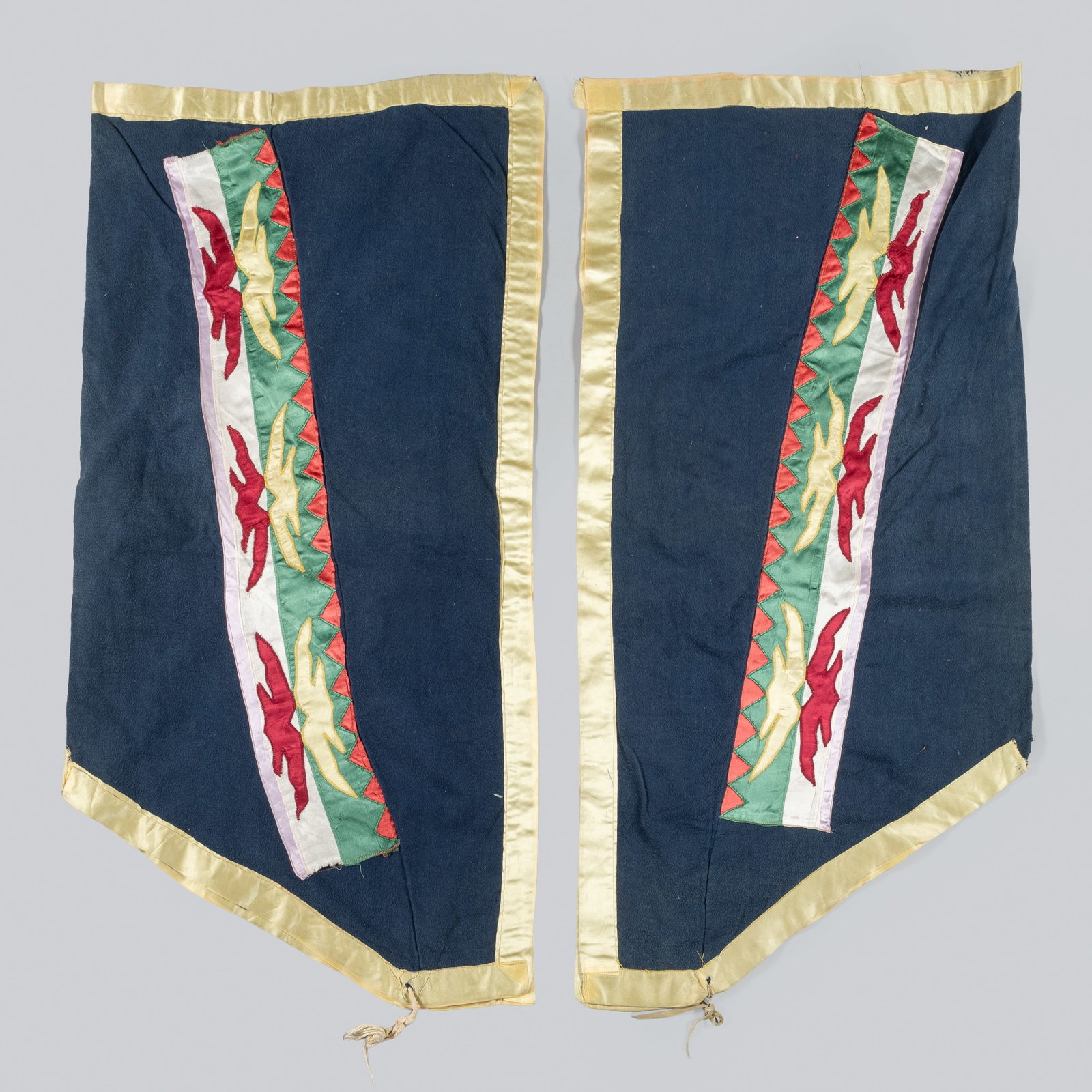 Osage Ribbonwork Leggings: Osage leggings feature the intricate, hand-stitched ribbonwork characteristic of the In-lon-schka dance traditions. Constructed from deep navy blue trade cloth, the leggings are adorned with vertical