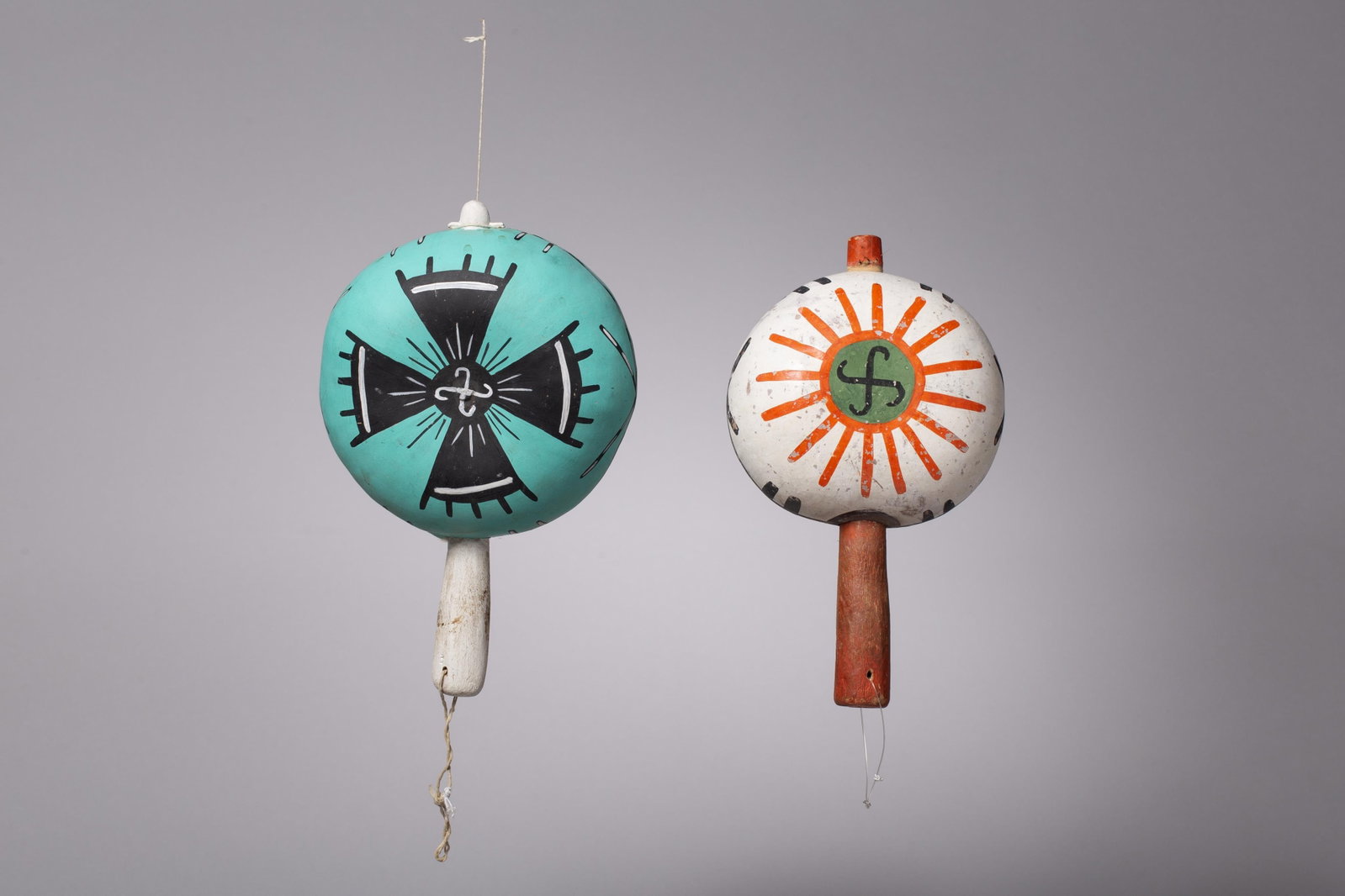 Pair of Hopi Rattles: The first rattle features a teal (turquoise) ground adorned with a black and white whirling log or migration cross motif. In Hopi culture, this four-armed pinwheel symbol represents the migrations of 