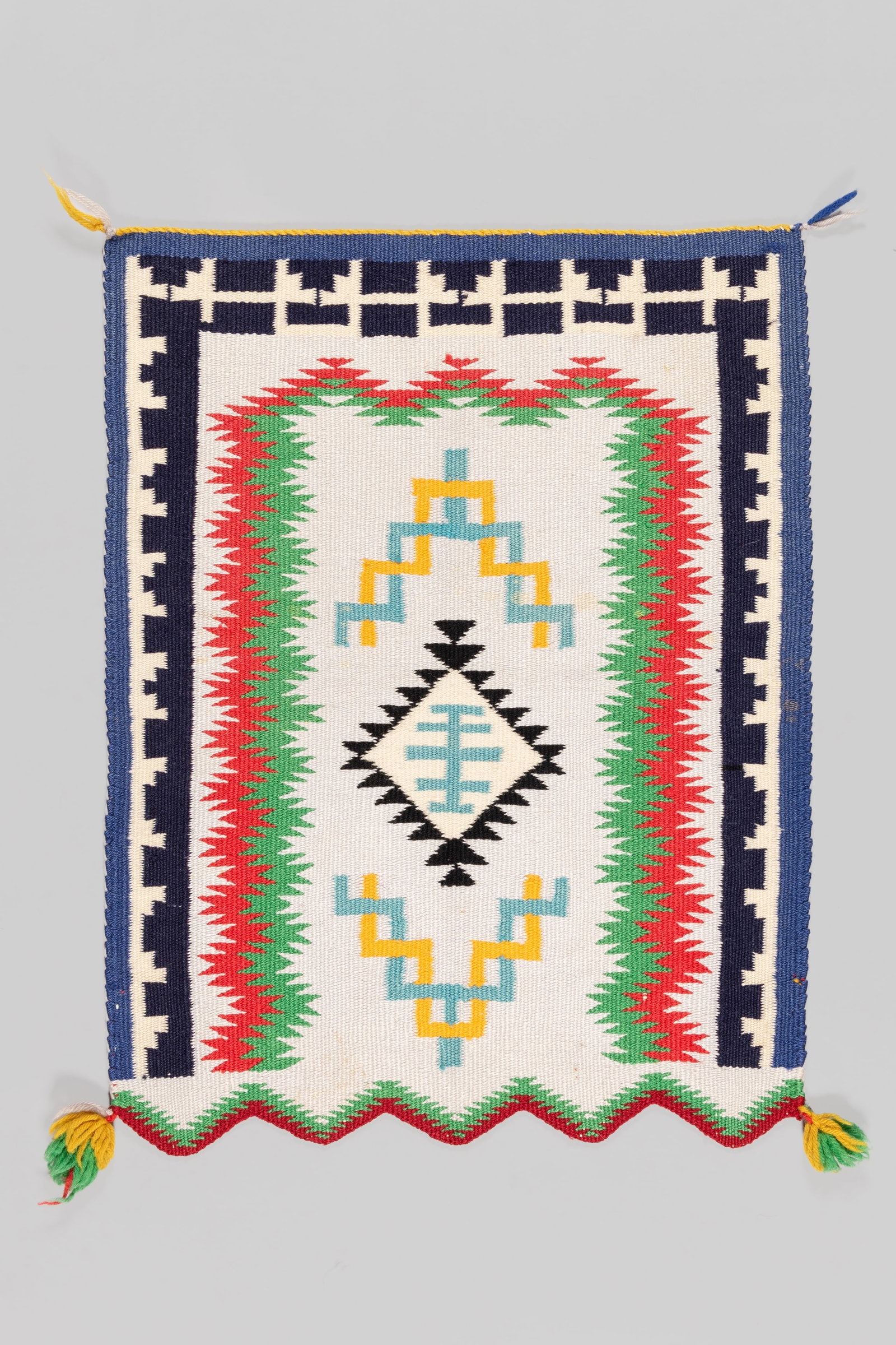 Navajo Germantown Weaving with Scalloped Edge, Ca. 1950s: This piece features a striking, multi-tiered geometric design utilizing a vibrant, high-contrast palette. The center presents a stacked serrated diamond motif rendered in golden yellow, turquoise blue