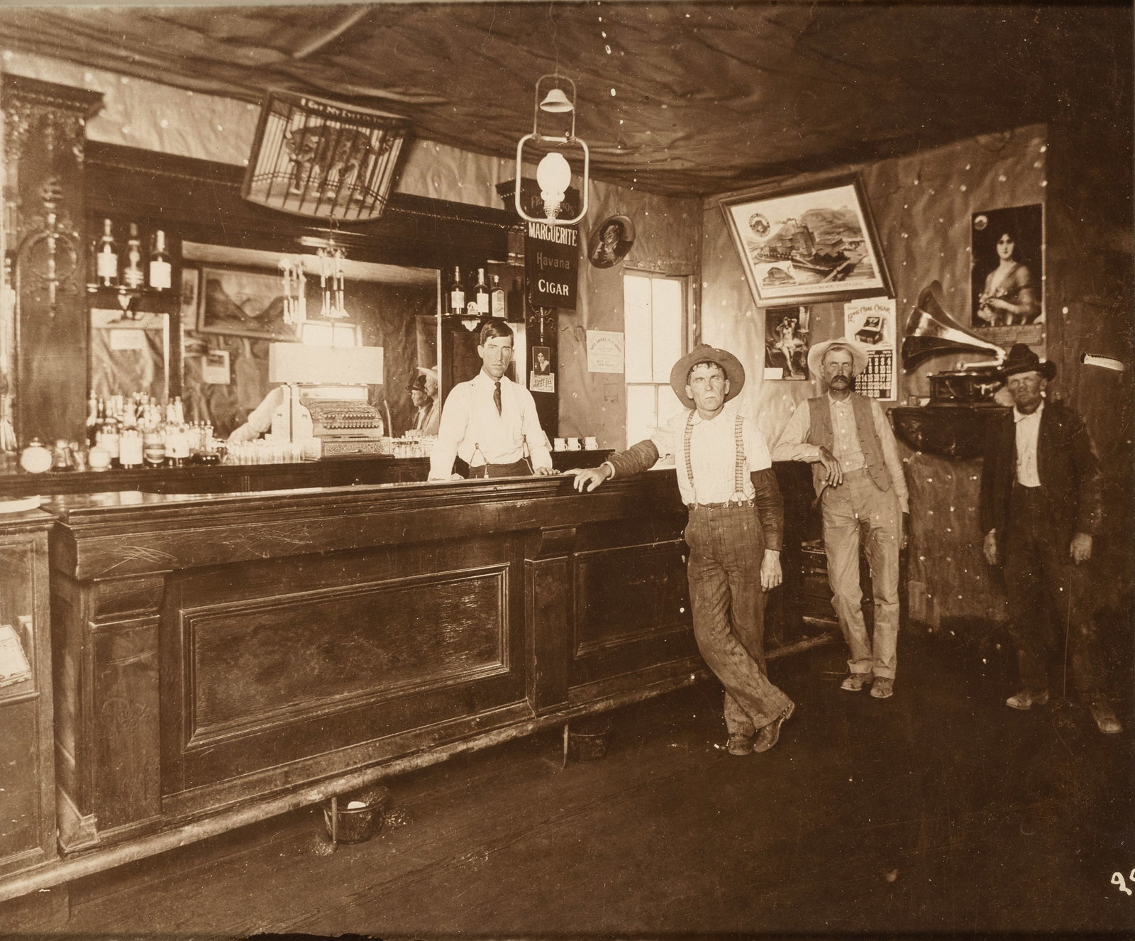 Framed The American Frontier - Interior Saloon Scene, Ca. 1890-1905: A rare and evocative reprint of a sepia-toned photograph capturing a candid moment within a late 19th or early 20th-century American West saloon. The composition features a long, paneled wooden bar—