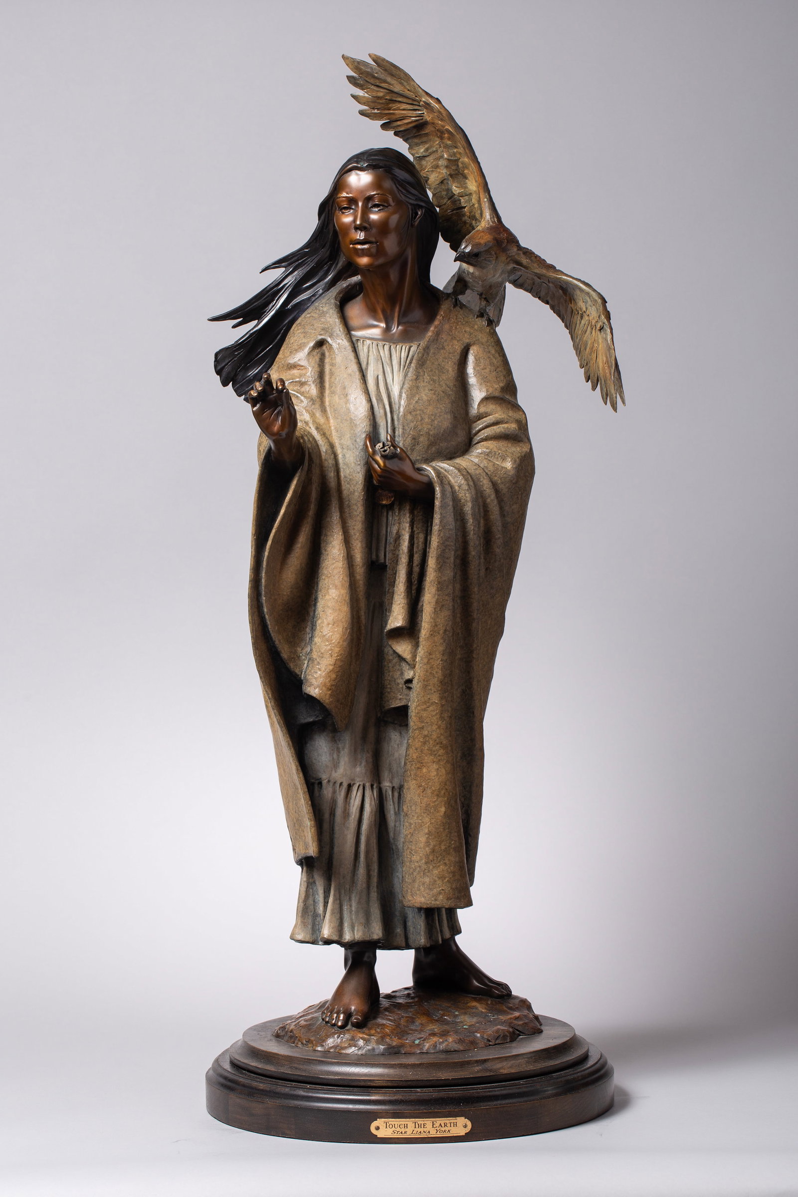 Star Liana York (b. 1952), Touch The Earth: signed and editioned on base 35/35Patinated bronze depicting a Native American woman holding out corn pollen, with a hawk perched on her shoulder, preparing for a prayer of blessing. Artist name and t