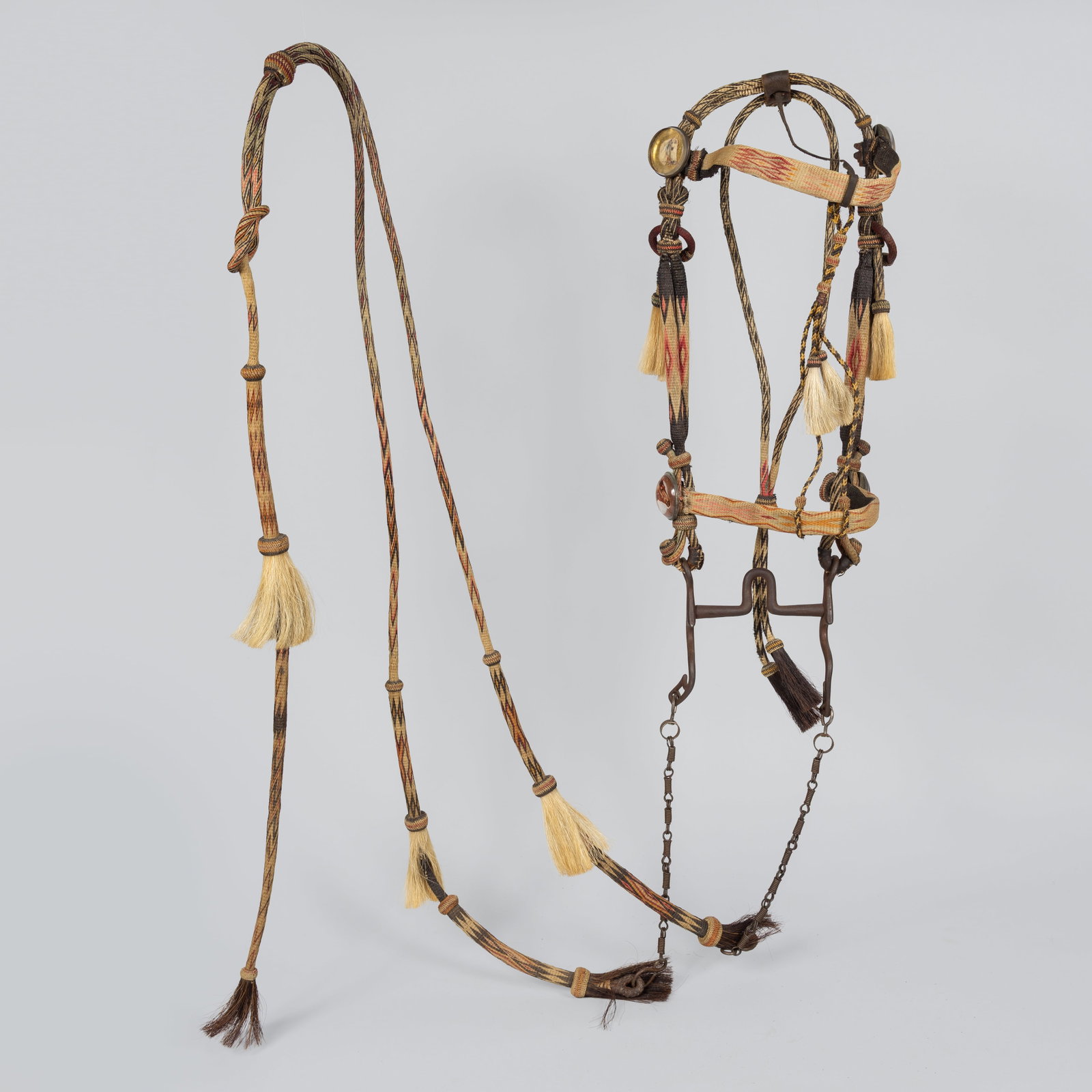 Deer Lodge Prison Bridle: A fine hitched horsehair bridle with the typical elements of Deer Lodge prison. Diamond and "X" patterns on a natural cream colored background and pink, red, green, yellow, and blue accents. Pink knot