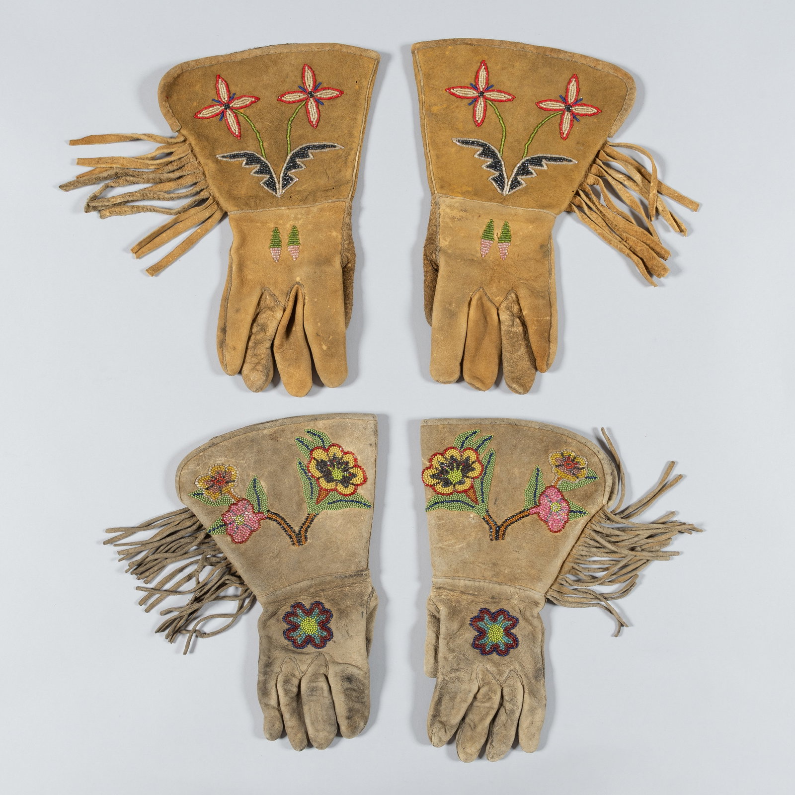 Two Pairs of Vintage Native American Beaded & Fringed Leather Gauntlet Gloves, Mid-20th Century: Offering of two distinct pairs of vintage Native American-style gauntlet gloves, showcasing traditional craftsmanship, leatherwork, and decorative beadwork.(A) Crafted from a warm, tan buckskin leathe