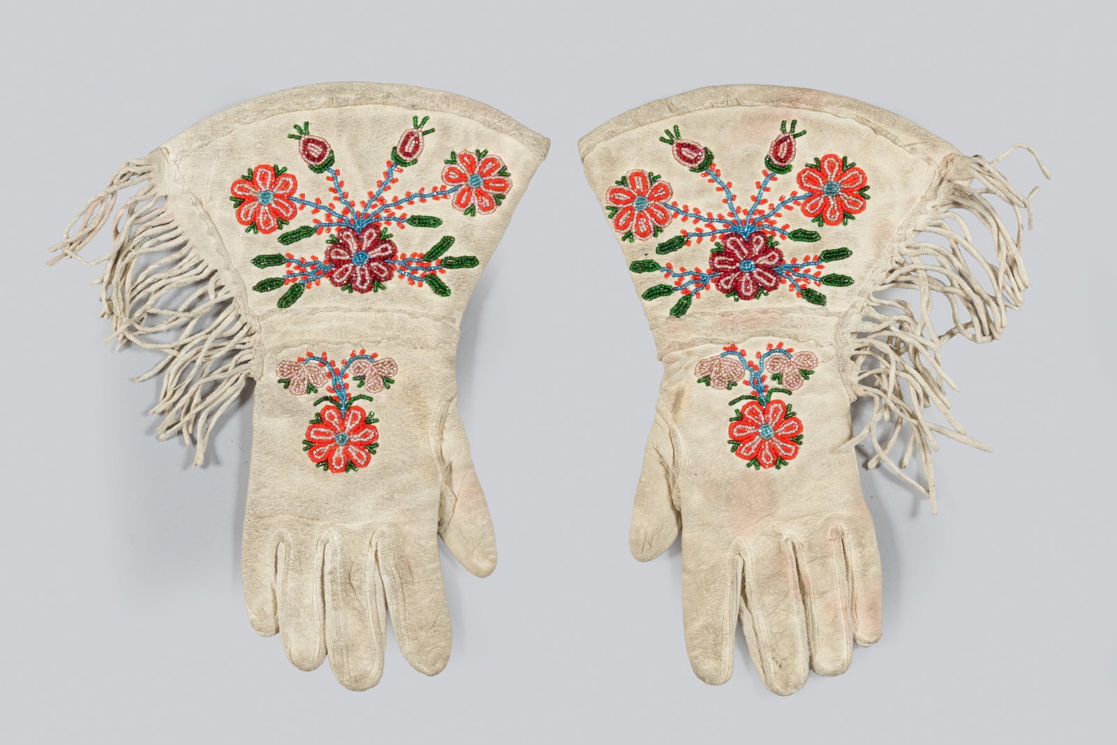 Vintage Native American Beaded Gauntlets: Constructed of soft tanned hide with long side fringe and colorful floral beadwork in red, blue, green, and pink seed beads. The cuffs are decorated with large radiating floral medallions flanked by