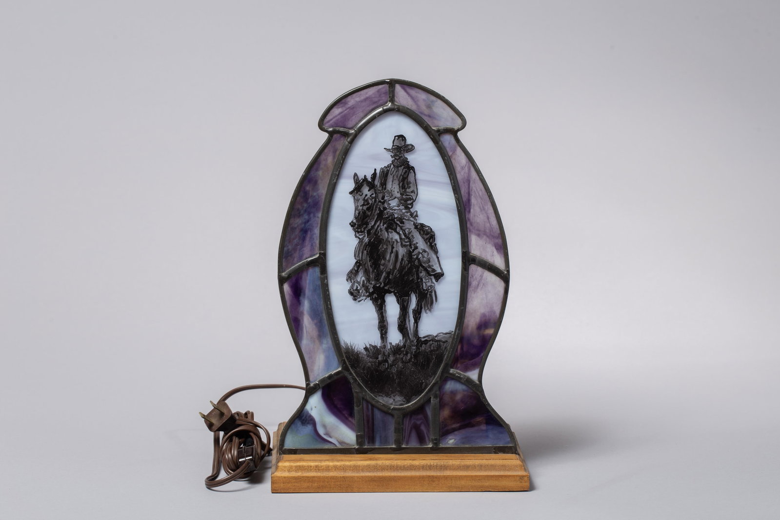 Vintage Stained Glass Cowboy Lamp: Ideal for cabin, lodge, or rustic southwestern interiors, this ambient accent piece features an eye-catching, multi-panel frame built with beautiful slag glass sections in deep hues of purple and blue