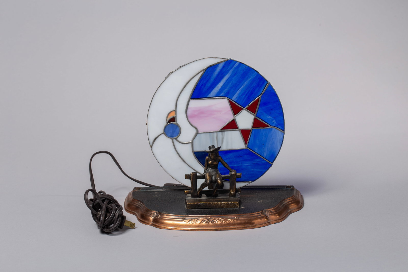 Vintage Stained Glass Cowgirl Lamp; Electric & One of a Kind: Striking, one-of-a-kind electric cowgirl accent lamp. This beautifully crafted piece features a detailed, bronze-finished sculptural base depicting a seated cowgirl in classic Western attire, resting 