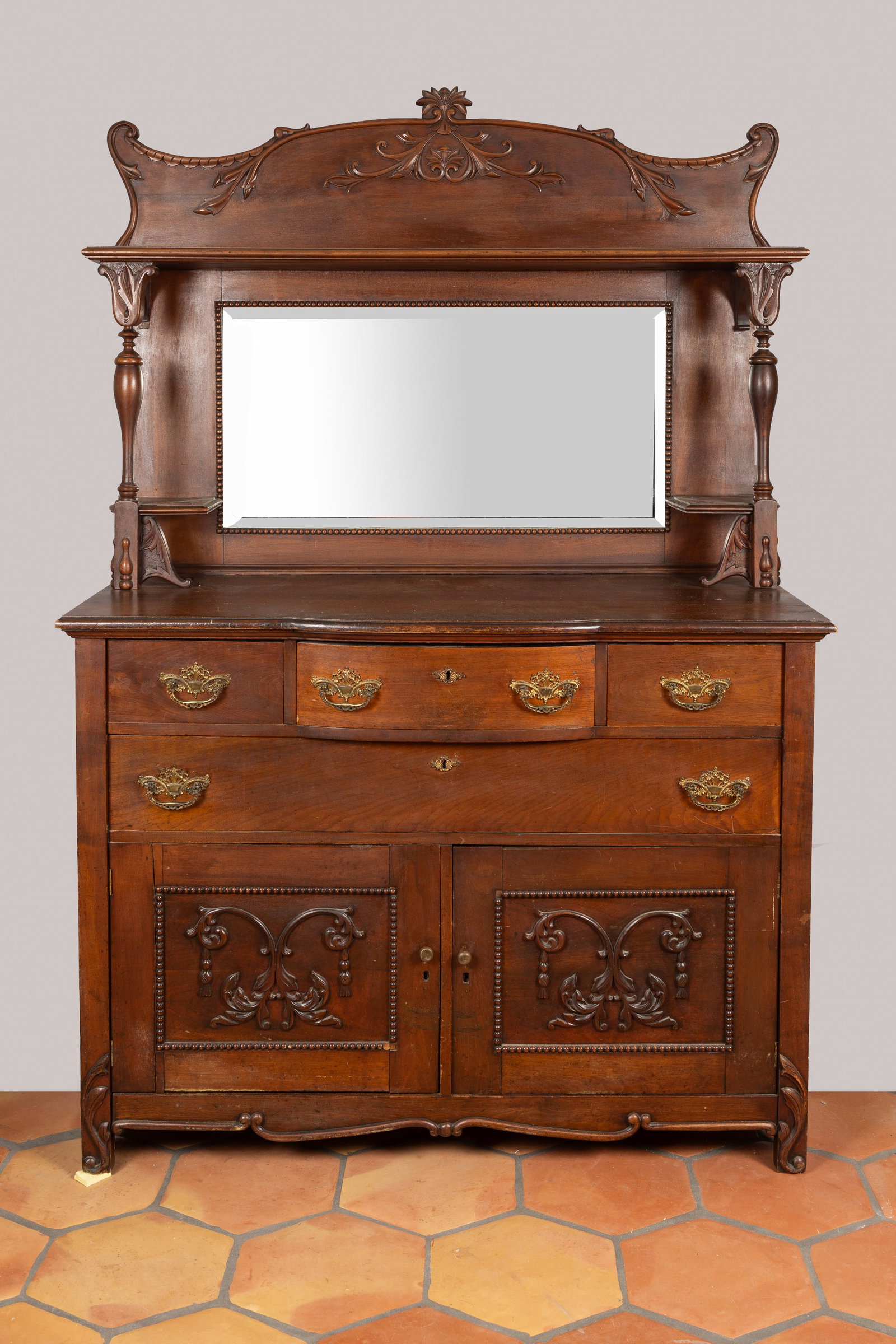 Antique Victorian Mirror-Back Oak Sideboard Buffet: An exceptional late 19th to early 20th-century Victorian-style two-piece oak sideboard buffet. The upper hutch features an ornately carved, scrolled crown above a central beveled mirror, flanked by ti