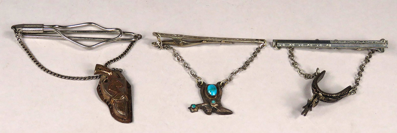 Collection of Three Vintage Western Tie Bars: Collection of Three Vintage Western Tie Bars. Sterling silver and 10k gold pistol and holster. Silver cowboy boot with inlaid turquoise. Engraved Silver Spur. Pistol and holster measure 1 3/4 inches.
