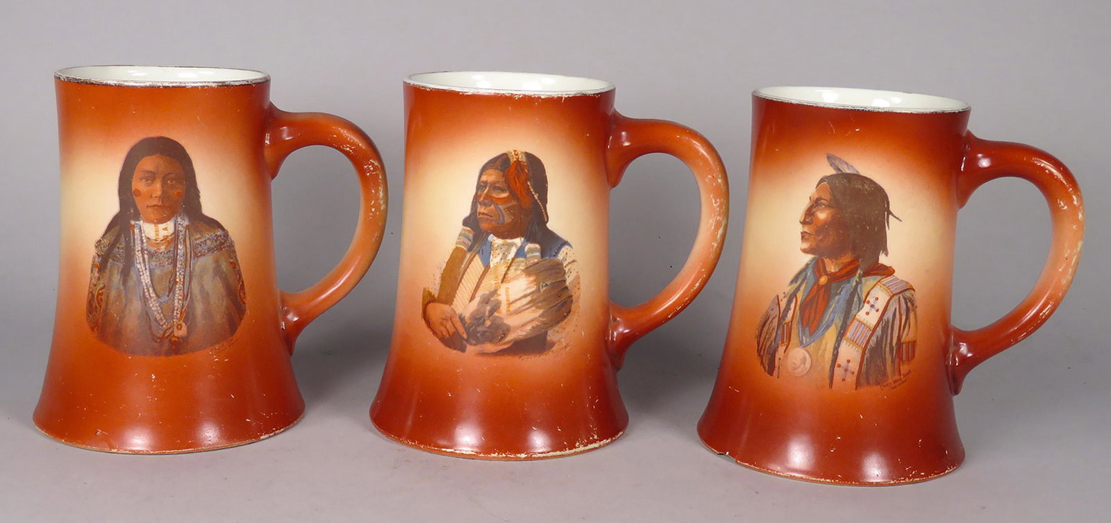 Three Native American Motif Porcelain Mugs: Three Native American Motif Porcelain Mugs. Image with kerchief has chip on bottom edge, overall paint wear. 5 inches tall.