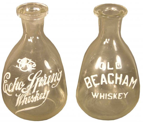 Two enamel label pinch bottles: Two enamel label pinch bottles, Echo Spring Whiskey and Old Beacham Whiskey. No chips or cracks. Aprox. 7 inches tall.