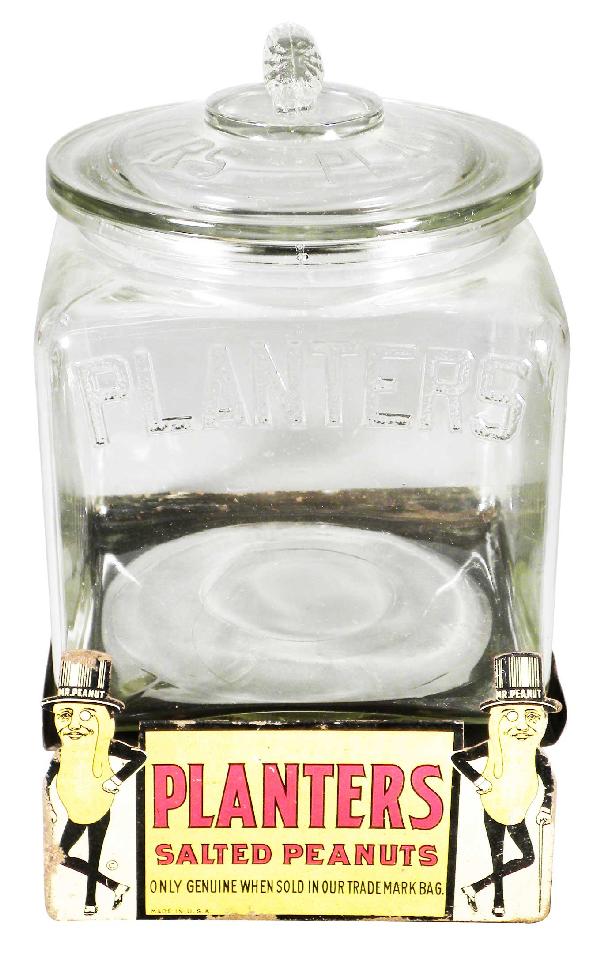 Planter's Peanut Store Jar w/original tin shelf ta: Planter's Peanut Store Jar with original tin shelf talker. Jar has tiny chip to lid otherwise excellent condition. Shelf talker has rust around edges otherwise good condition. 7 1/4 X 9 X 7 1/2 inches