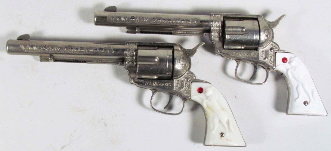 Two Nichols Stallion 45 Die Cast Toy Cap Guns: Two Nichols Stallion 45 Die Cast Toy Cap Guns, ca. 1950. Pasadena, TX. White plastic handles have embossed Stallion and red jewel. Wagon train embossed on 5 3/4 inch barrels. Very good condition.