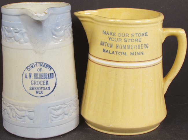Two Grocer Advertising Stoneware Pitchers: Two Grocer Advertising Stoneware Pitchers. A.W. Hildebrand, Sheboygan, Wis. With embossed cherry design, small chip in spout lid. Red Wing Saffron Ware for Anton Hommerberg, Blaton, Minn. No chips or 