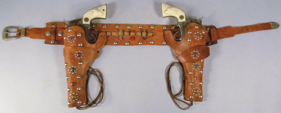 Pair of Hubley Cowboy Toy Cap Guns in Gun Rig: Pair of Hubley Cowboy Toy Cap Guns in Gun Rig. Studded leather holder with red/green/amber studs. Guns in excellent condition.