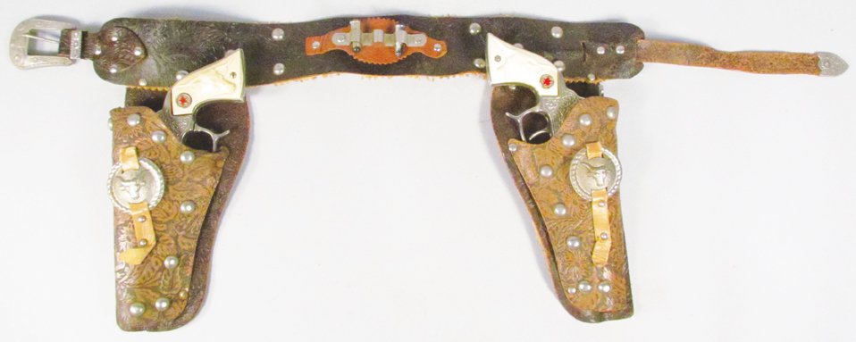 Pair of Hubley Texan Toy Cap Guns in Gun Rig: Pair of Hubley Texan Toy Cap Guns in Gun Rig. Two toned hand tooled leather with steer head conchos. Guns have normal playwear.