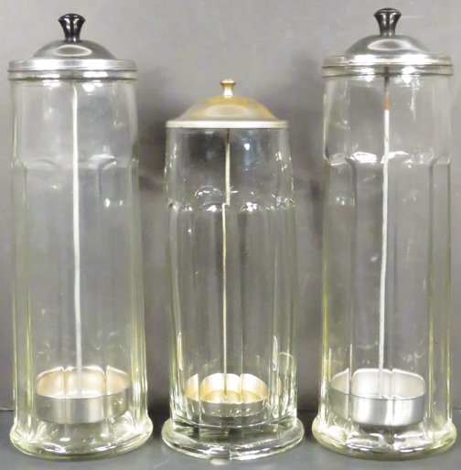 Trio of Soda Fountain Straw Holders: Trio of Soda Fountain Straw Holders. Pressed glass, large holders have aluminum lids, small holder has nickel plated brass lid. All have original lifts. No chips or cracks. Tallest measure 13 inches.