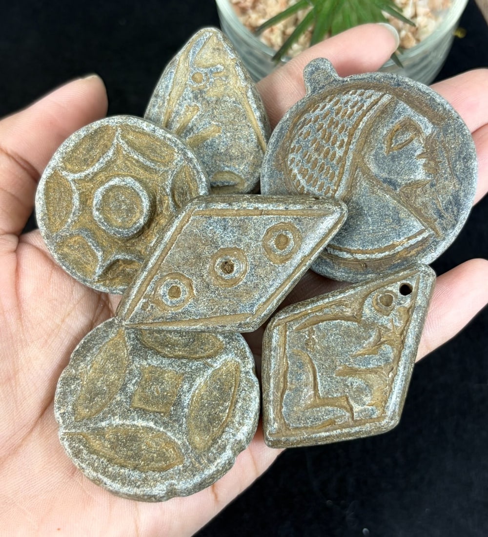 Lot of 7 Ancient Carved Schist Stone Amulet Pendants, 46YD: This seven-piece antiquity grouping features hand-carved talismans crafted from weathered grey schist stone with natural aged ochre patina across all surfaces. Shapes vary including round, teardrop, d