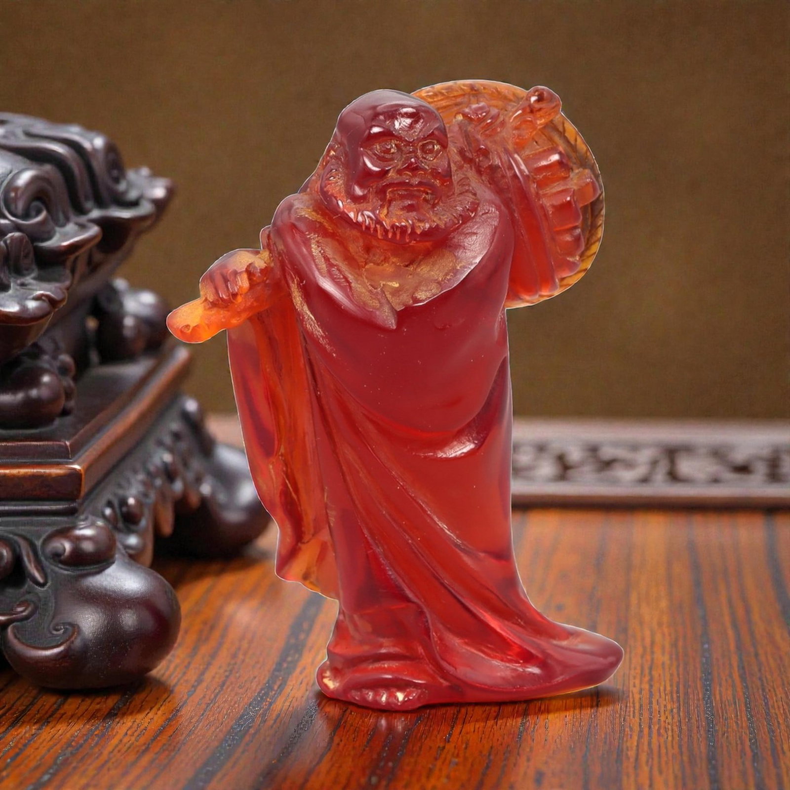 A Chinese Amber-Resin Figure of a Luohan, 20th Century, 41FH: Cast or carved from translucent amber-colored red resin with internal tonal variation, scattered inclusions, and minor entrapped bubbles, the figure represents a standing luohan shown holding a staff 