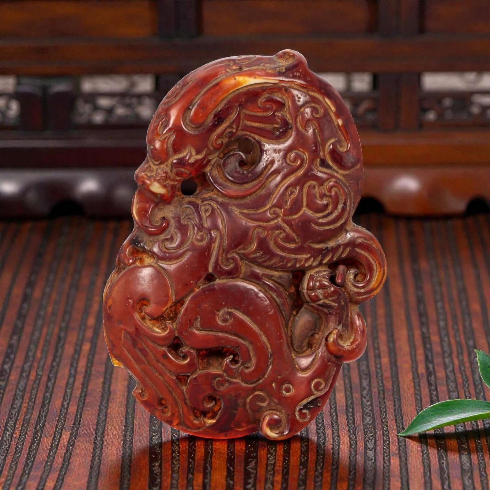 A Chinese Amber-Resin Openwork Plaque Pendant, 90FC: Molded and carved from translucent reddish-brown amber-colored resin with areas of lighter translucency and surface variation, the object is worked as an irregular plaque featuring a stylized mask-lik