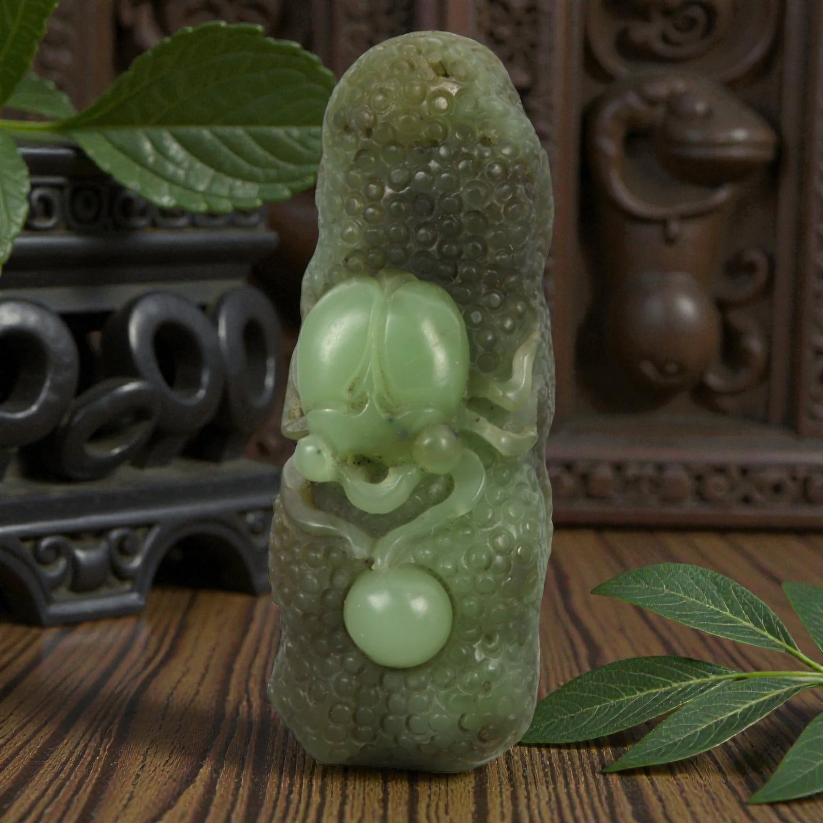 A Chinese Nephrite Jade Spider-and-Fruit Pendant, 20th Century, 12FB: Carved from green nephrite jade with darker mottling and areas of translucency, the pendant is modeled as an elongated fruit with a densely textured surface composed of rounded nodules. The front is c