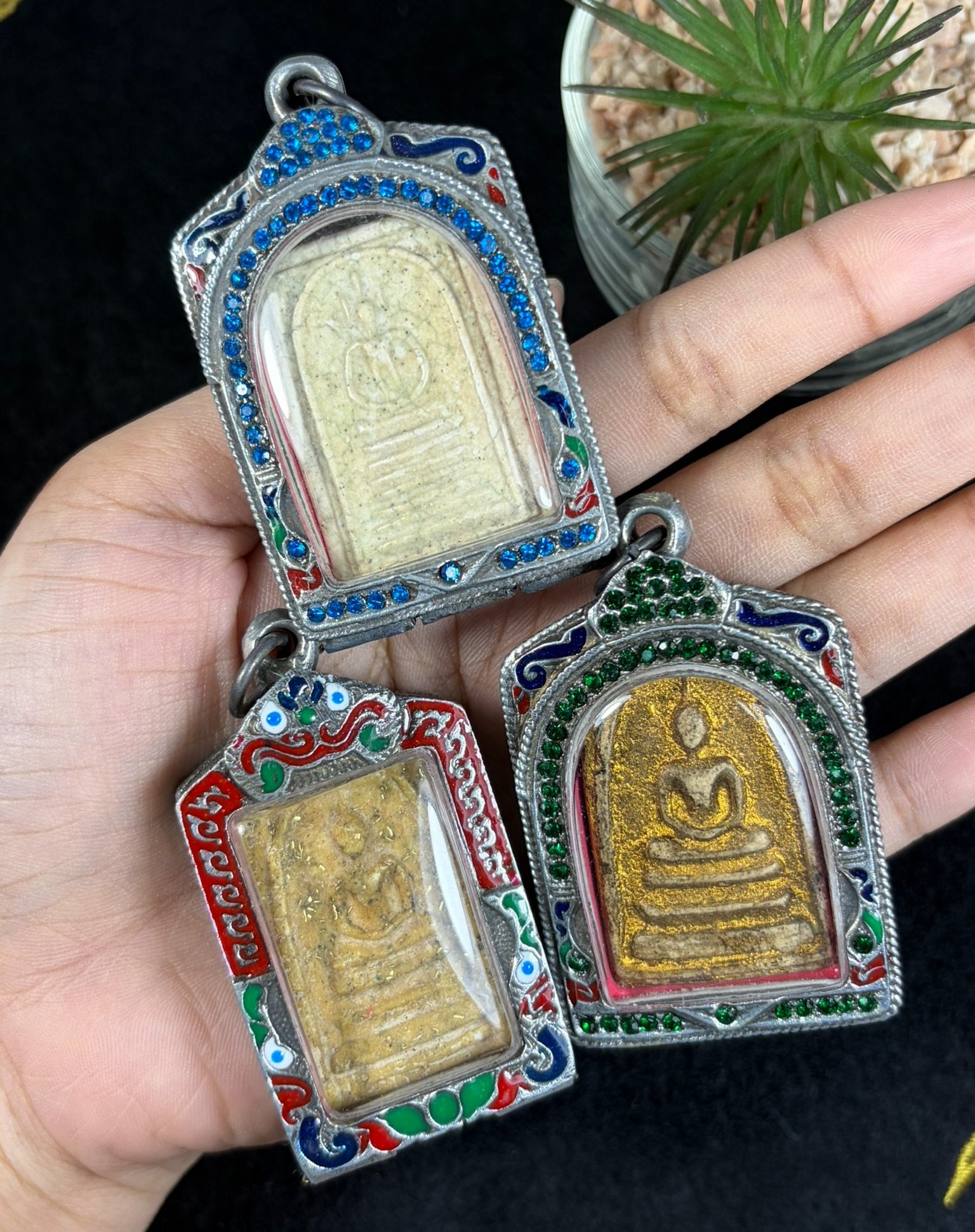 Vintage Thai Enamel Crystal Cased Buddha Amulets - 3 Piece Religious Lot, 93AR: This set includes three vintage Thai Buddhist votive amulets secured within untested silvered metal protective casings fitted with clear viewing windows and top suspension loops for pendant wear. Each