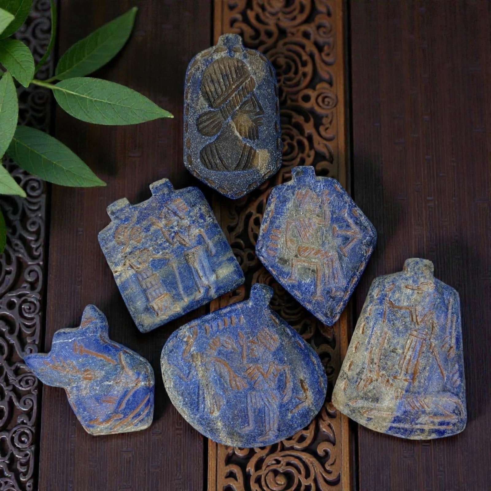 A Lot of 6 Ancient Near Eastern Lapis Lazuli Amulets, 9AC: The group comprises six amulets carved from lapis lazuli, displaying rich blue tones with natural white and grey inclusions, alongside surface patina and wear consistent with antiquity. Each piece fea