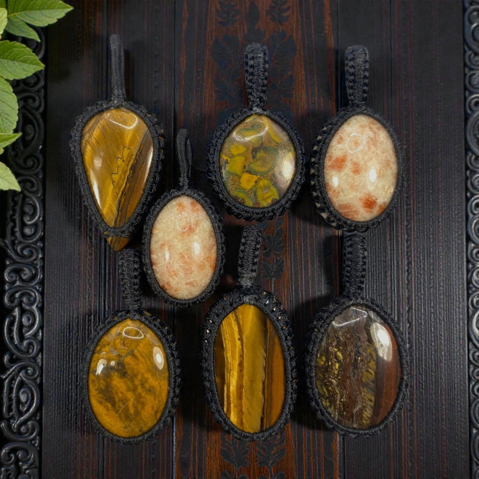A Lot of 7 Macrame-Wrapped Gemstone Pendants, 9WS: This lot includes seven handcrafted macrame-wrapped gemstone pendants, each measuring 4-5 cm in height. The collection features varied natural stones, including tiger's eye, sunstone, and a patterned 