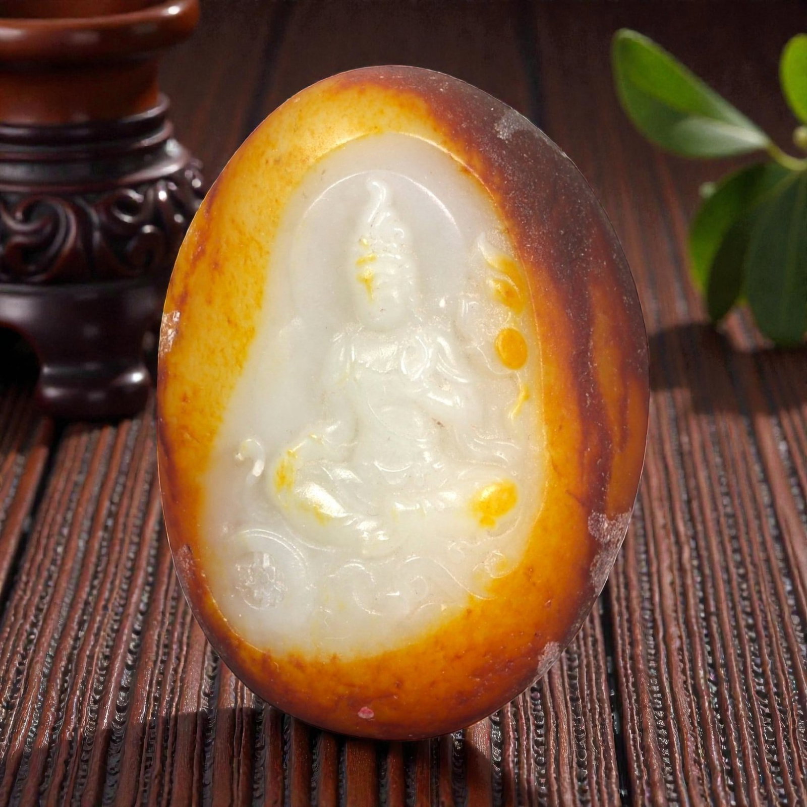 A Chinese Xinjiang Hetian Jade Buddha Carving, 54FB: Carved from bi-colored jade with a creamy white interior and a surrounding russet-brown skin, the plaque is oval in form and worked in shallow relief. One face depicts a seated Buddha shown frontally,