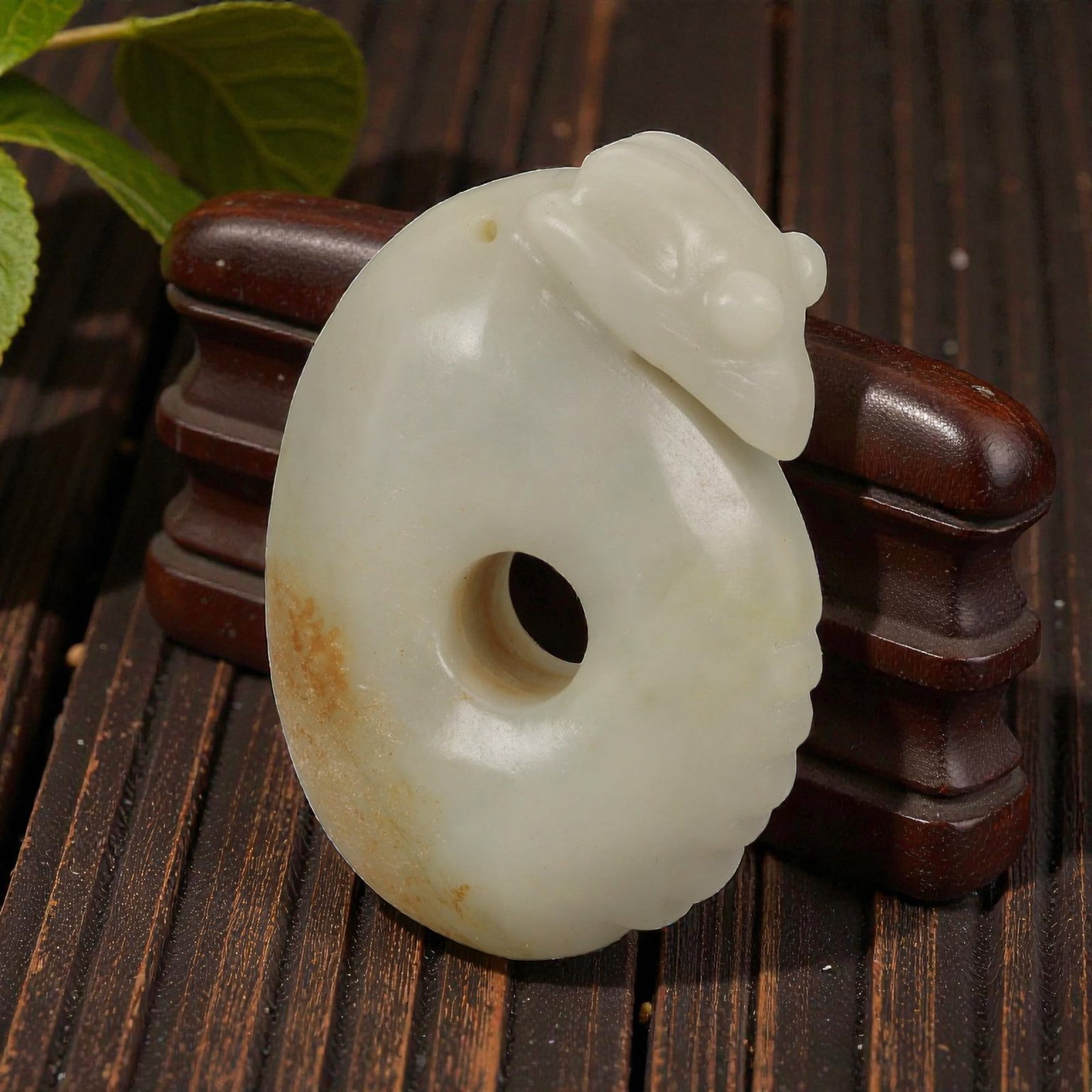 A Chinese Hetian Nephrite Jade Pendant, 56YB: Carved from pale creamy-white Hetian jade with areas of natural russet coloration, the pendant is worked as a thick oval form pierced by a circular central aperture. One side is carved in low relief w