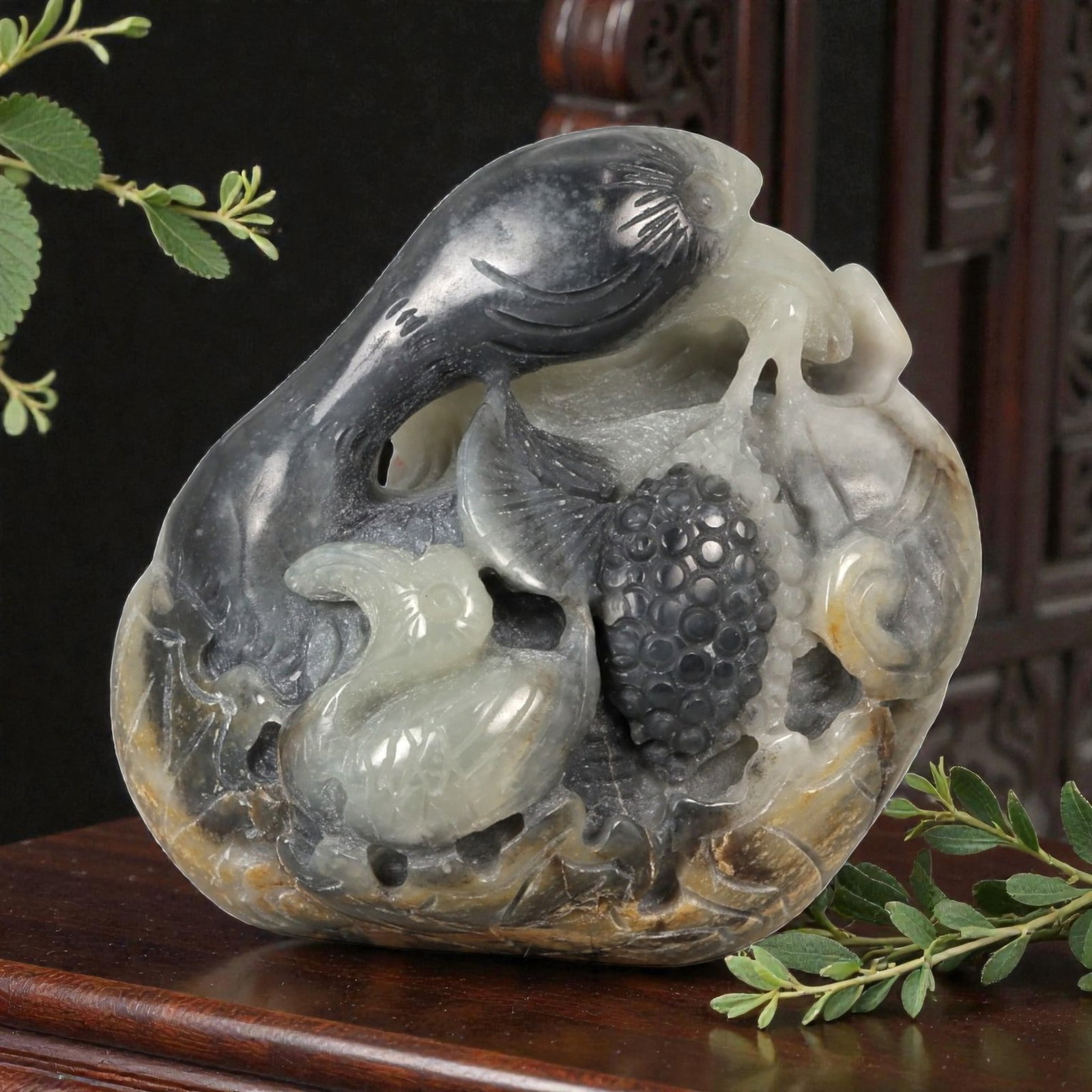 A Chinese Hetian Nephrite Jade Carving of Birds and Grapes, 20th Century, 22FD: Carved from a naturally variegated pebble of Hetian nephrite jade, the sculpture is worked in high relief and openwork to depict a lively scene of birds amidst fruiting vines. Two birds, their bodies 