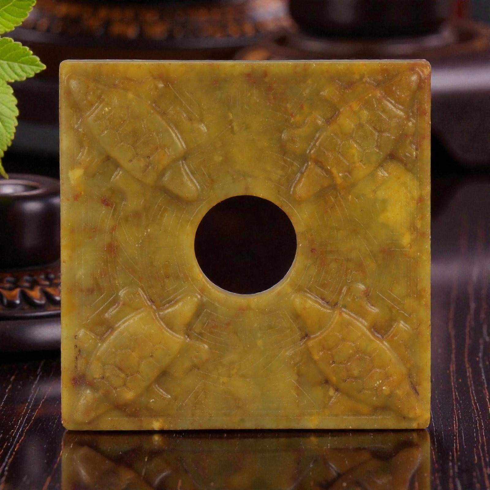 A Chinese Hardstone Plaque with Central Aperture, 20th Century, 77FD: A square hardstone plaque carved from mottled yellow-brown stone with russet inclusions and subtle surface translucency. The plaque is centered by a circular aperture, around which the surface is work
