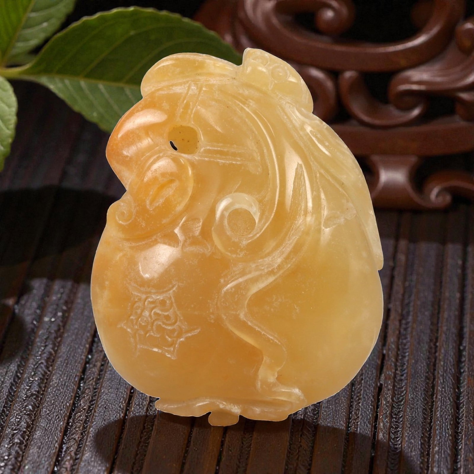 A Chinese Amber-Colored Hardstone Pendant with Zoomorphic Mask, 20th Century, 80FC: Carved from an amber-colored translucent hardstone or composite material, the pendant is worked in relief as a stylized zoomorphic mask, likely drawing on lion or mythical beast imagery. The form is c