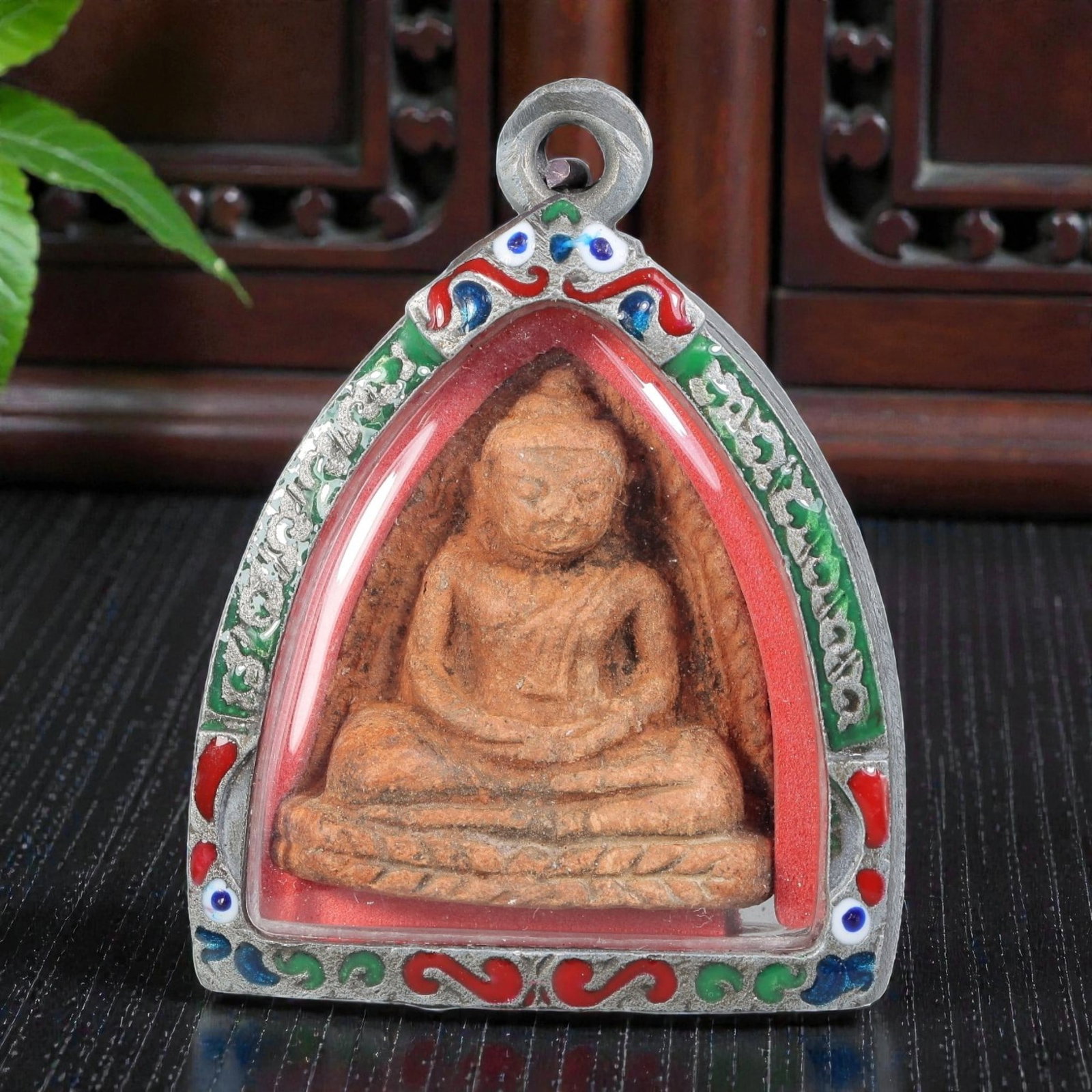 Thai Seated Buddha Amulet - Triangular Enamel Silver Tone Pendant, 68ZB: A Thai Buddhist amulet featuring a terracotta-colored seated Buddha figure, housed in a triangular silver-tone metal casing with colorful enamel detailing. The glass-fronted enclosure protects the han
