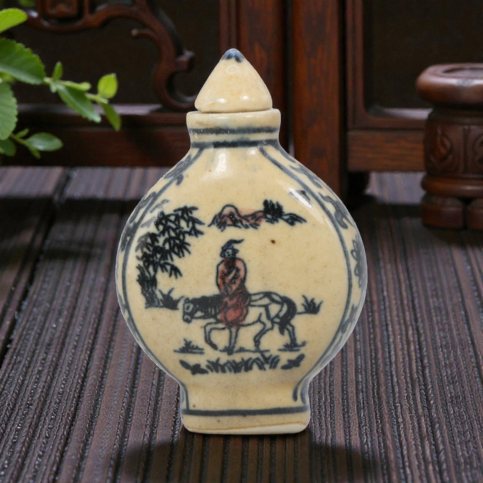A Chinese Porcelain Snuff Bottle, 20th Century, 7YD: Crafted from porcelain with a pale cream glaze and decorated in underglaze blue with copper red accents, the snuff bottle features a flattened, rounded body, a short cylindrical neck, and a conical st