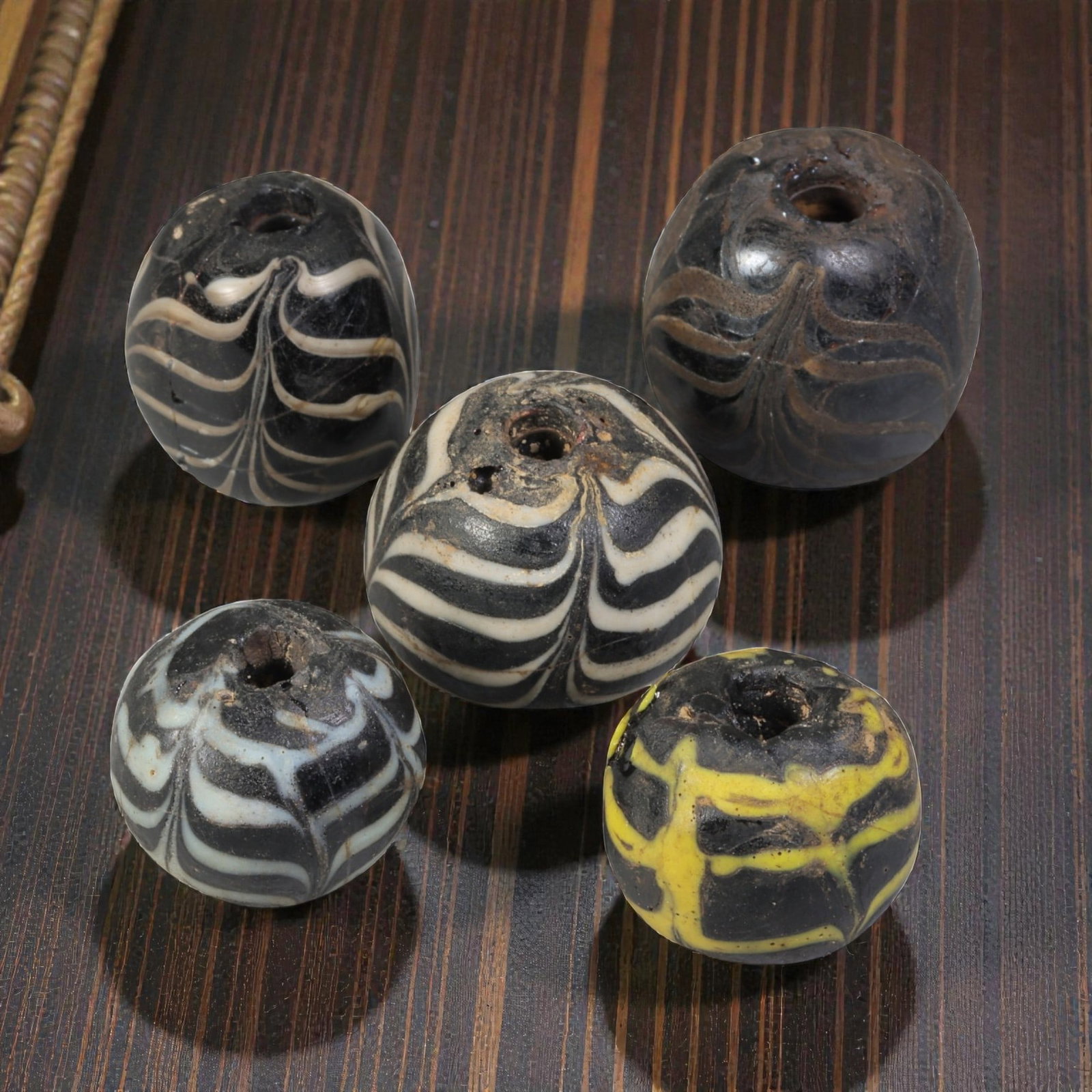 Lot of 5 Antique Islamic Feather-Patterned Glass Beads, Circa 9th-14th Century, 39WM: A group of five spherical glass beads, each with a central perforation. The beads feature characteristic feather-patterned decoration, created by trailing contrasting coloured glass over a dark base. 