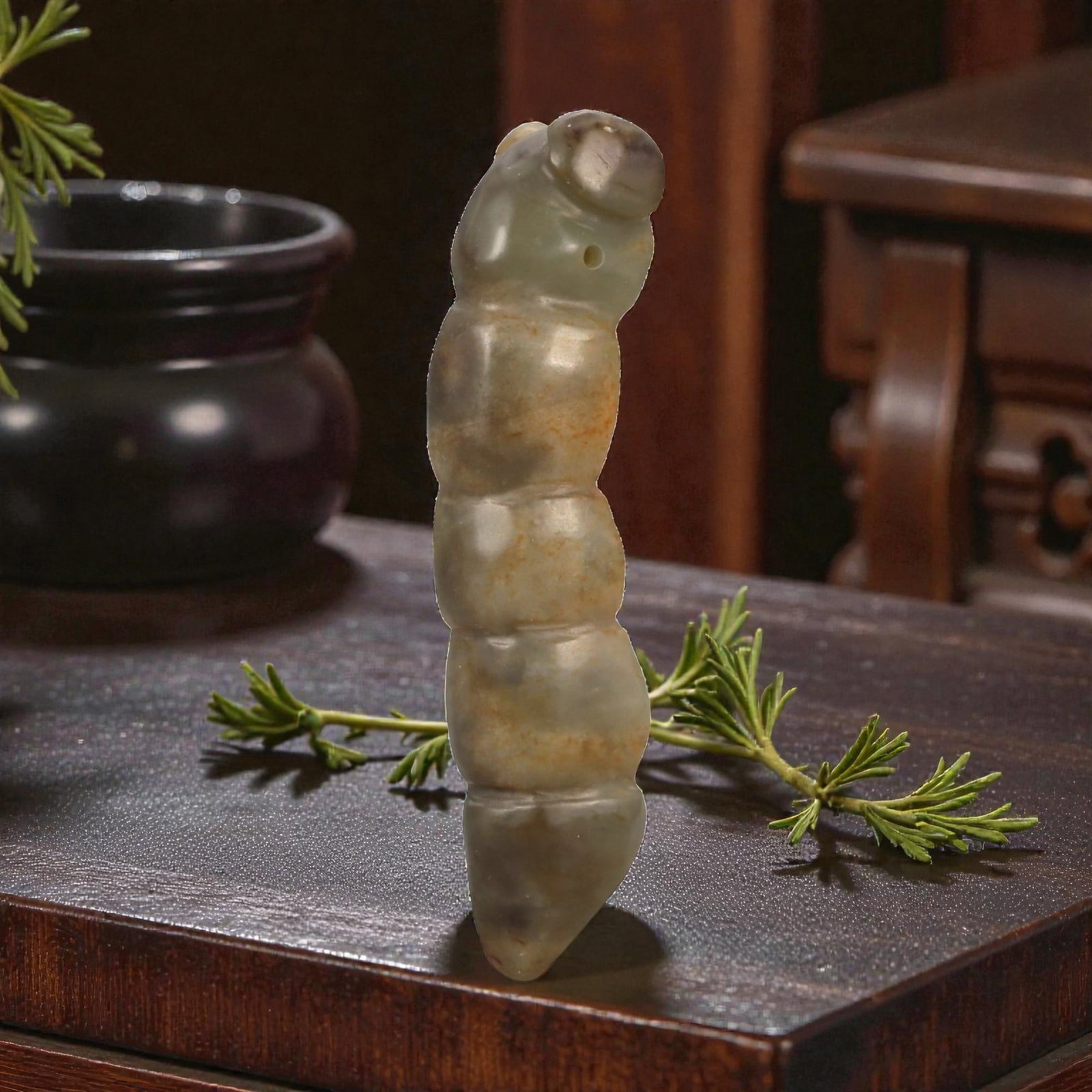 A Chinese Jade Worm Carving Pendant, Late Qing Dynasty, 64FB: Carved from mottled jade with grey-green tones and areas of brownish mineral inclusions, the object is modeled in the round as a stylized worm or larval form. The body is elongated and vertically orie